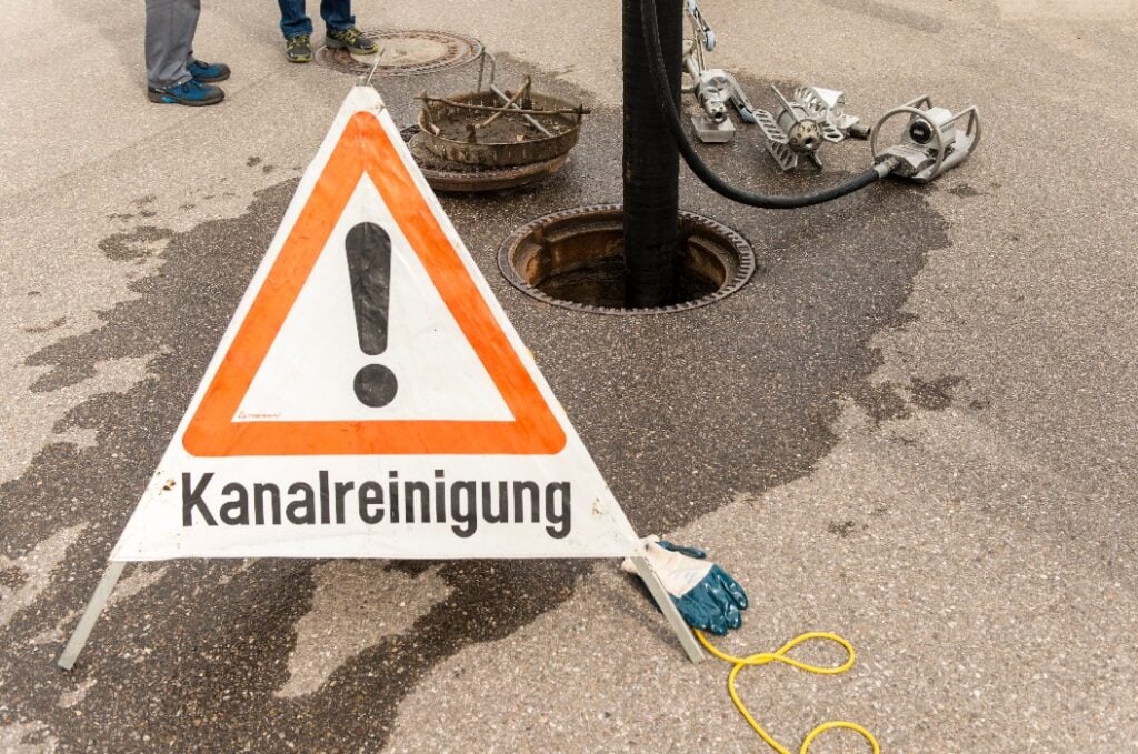Offener Kanaldeckel und Warnschild für Kanalsanierung