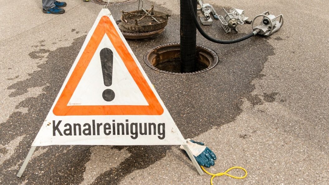 Offener Kanaldeckel und Warnschild für Kanalsanierung